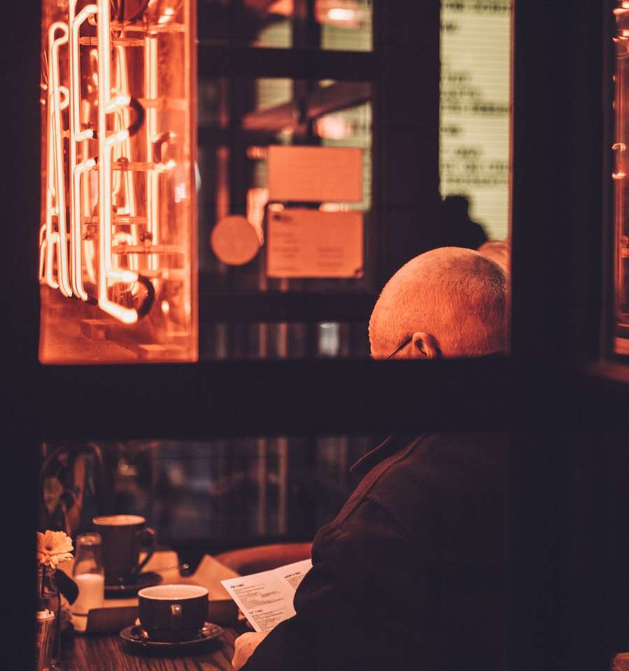 muž sedí na židli a čte knihu před stolem skládačky online