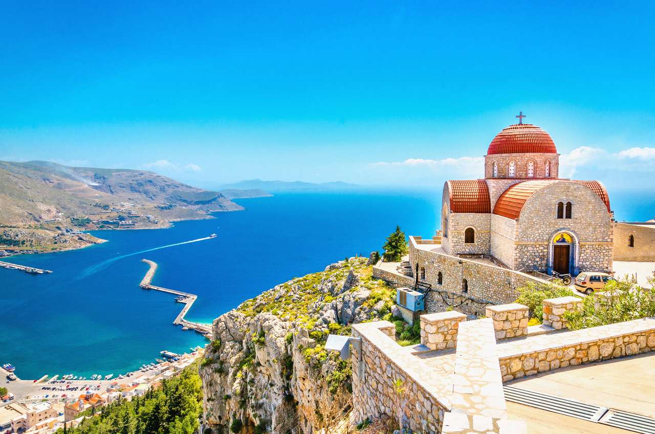 Vizualizare uimitoare asupra bisericii de la distanță cu acoperiș roșu pe stânca mării, Grecia puzzle online