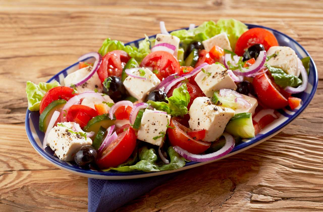 Страва здорового свіжого грецького салату з сиром фета, оливками, огірком, листям салату, цибулею та помідорами, приправленими зеленню на дерев'яному столі пазл онлайн