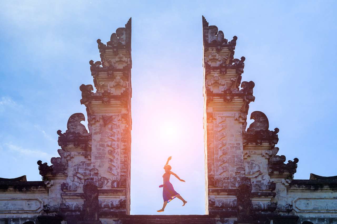 Kvinna resenär hoppar med energi och vitalitet i porten av ett tempel, Bali, Indonesien Pussel online
