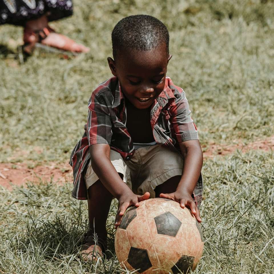 улыбающийся мальчик сидит, держа футбольный мяч в дневное время пазл онлайн