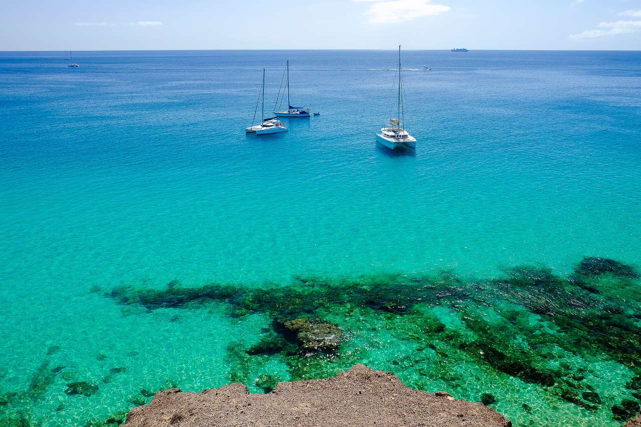 Pohled na oceán s křišťálovou vodou a třemi wtististickými čluny v Morro Jable na Kanárském ostrově Fuerteventura, Španělsko. skládačky online