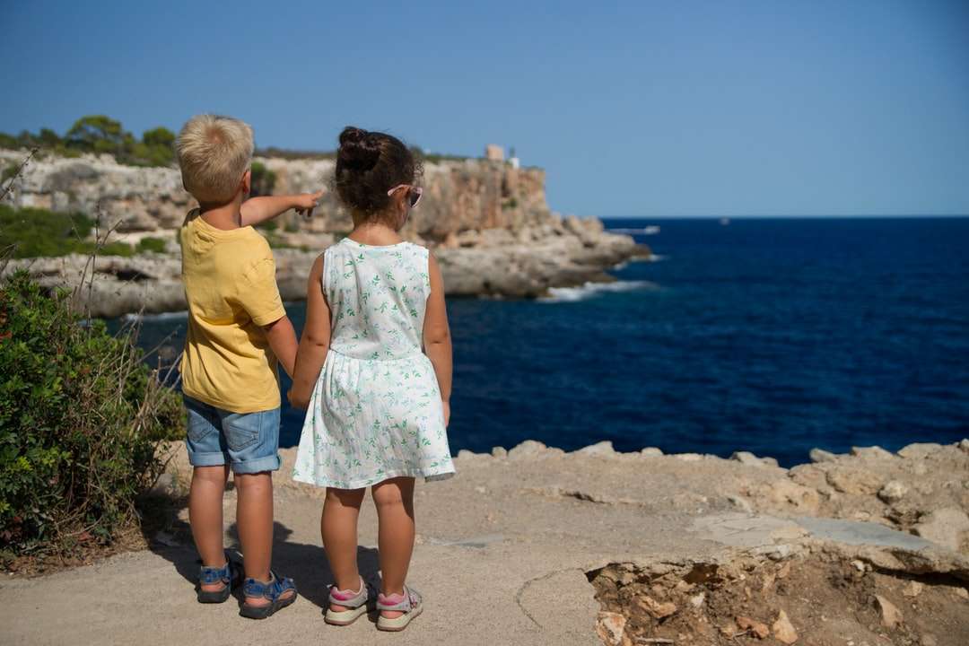двое детей стоят у скалы и смотрят на океан пазл онлайн