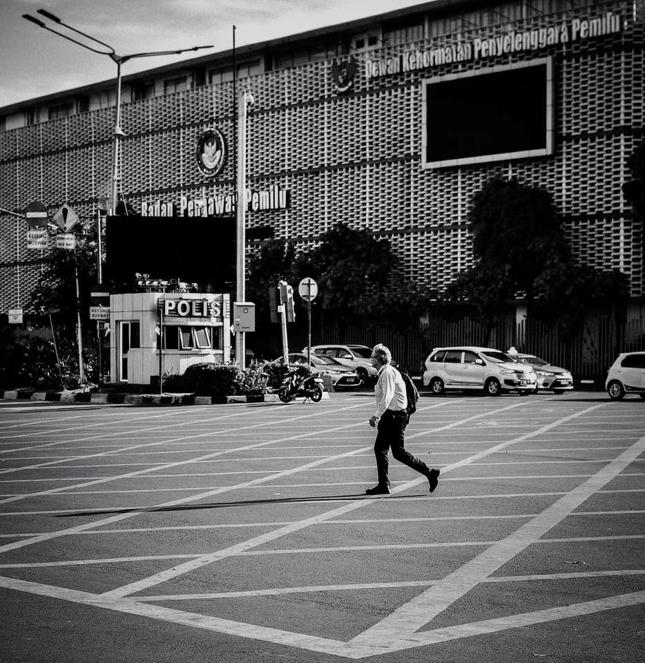 foto in scala di grigi di un uomo che cammina accanto all'edificio puzzle online