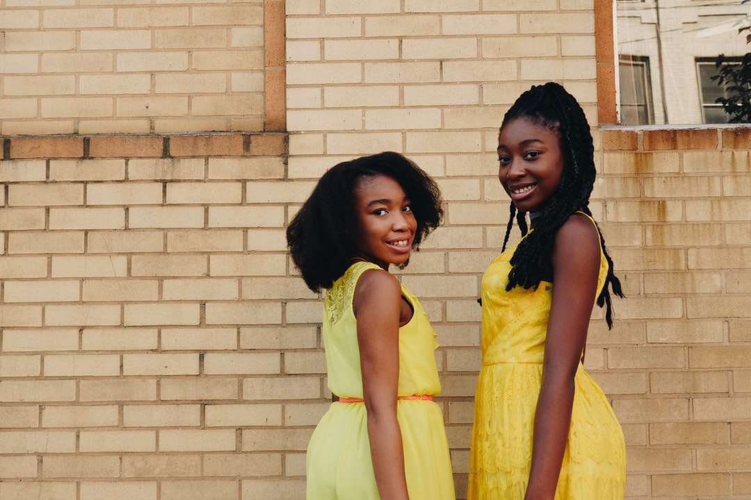 Due donne che indossano abiti da giallo senza maniche vicino a mattoni marroni puzzle online