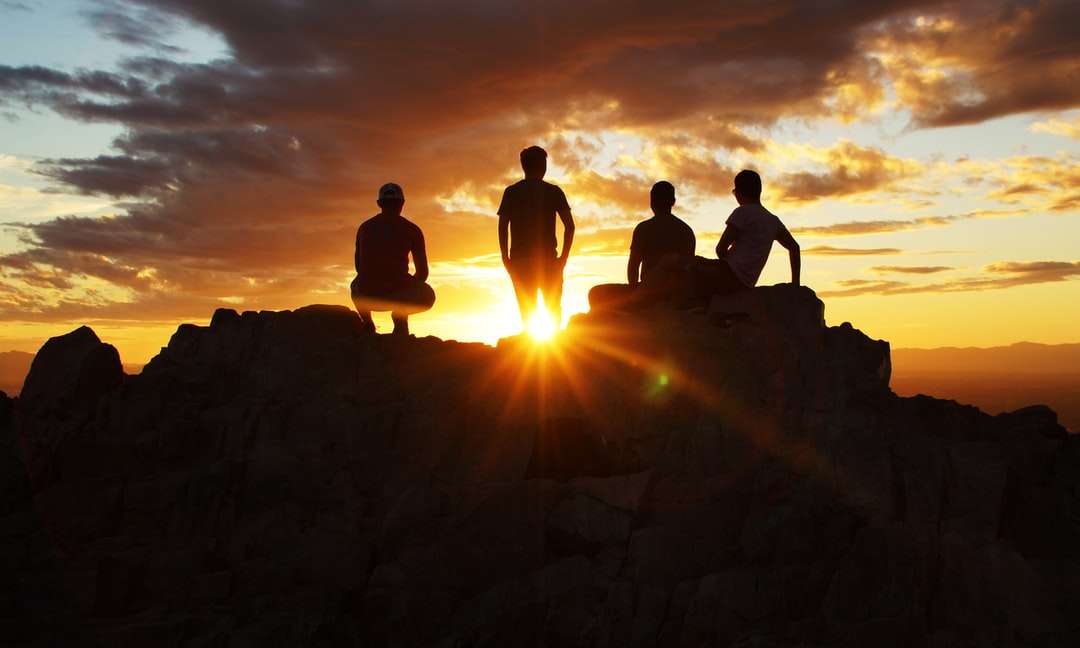 siluettfotografering av fyra personer på klippan under solnedgången Pussel online
