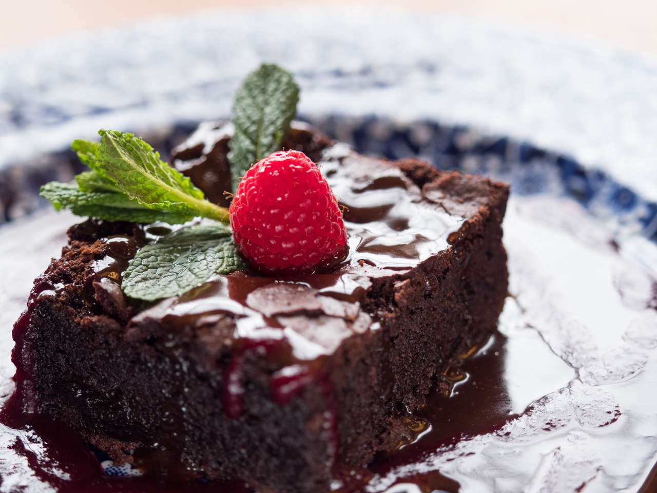 Närbildsskiva av chokladkaka serveras på en tallrik med chokladsås. Raspberry frukt och mynta löv på toppen. Naturligt ljusfönster. pussel på nätet