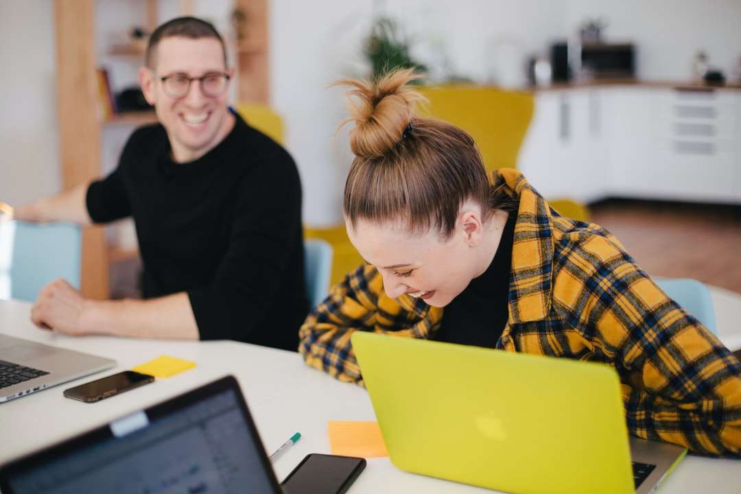 bărbat și femeie râzând în timp ce stau în fața laptopurilor puzzle online