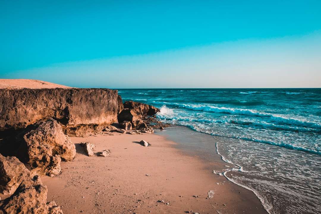 brun stenig strand nära vattenkroppen under dagtid Pussel online