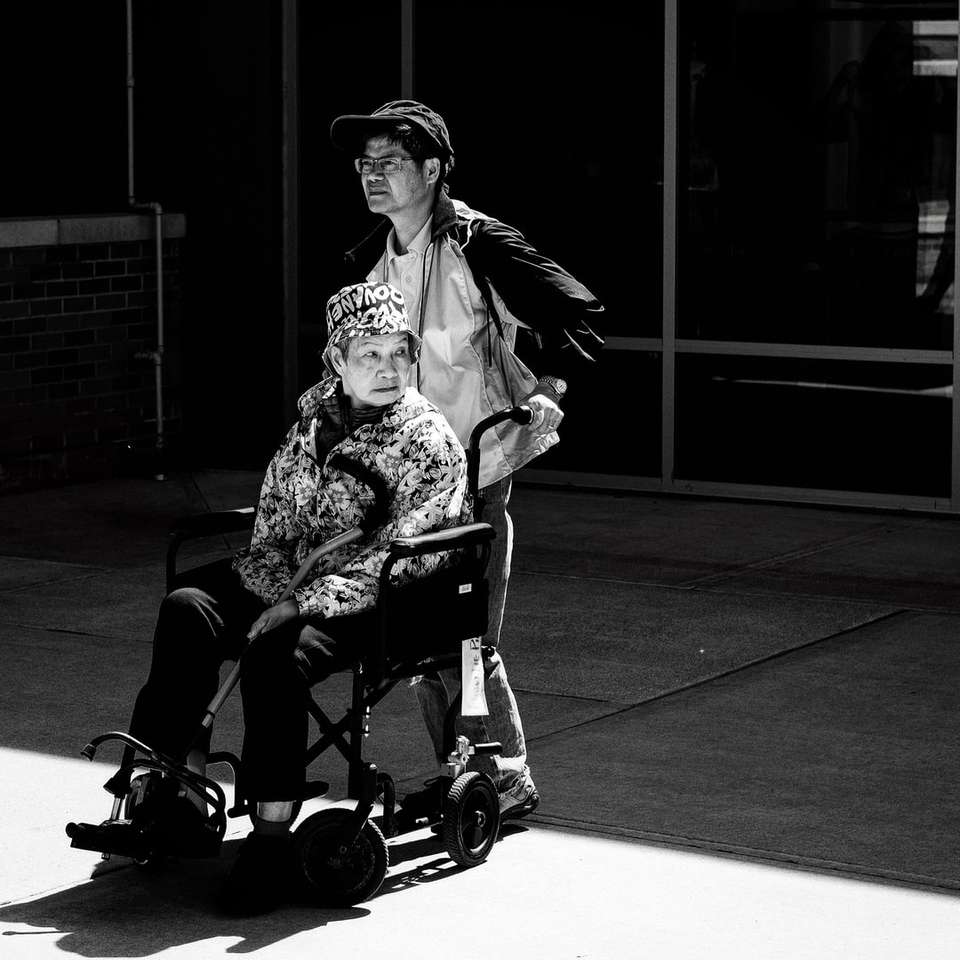 foto en escala de grises de un hombre empujando una silla de ruedas rompecabezas en línea