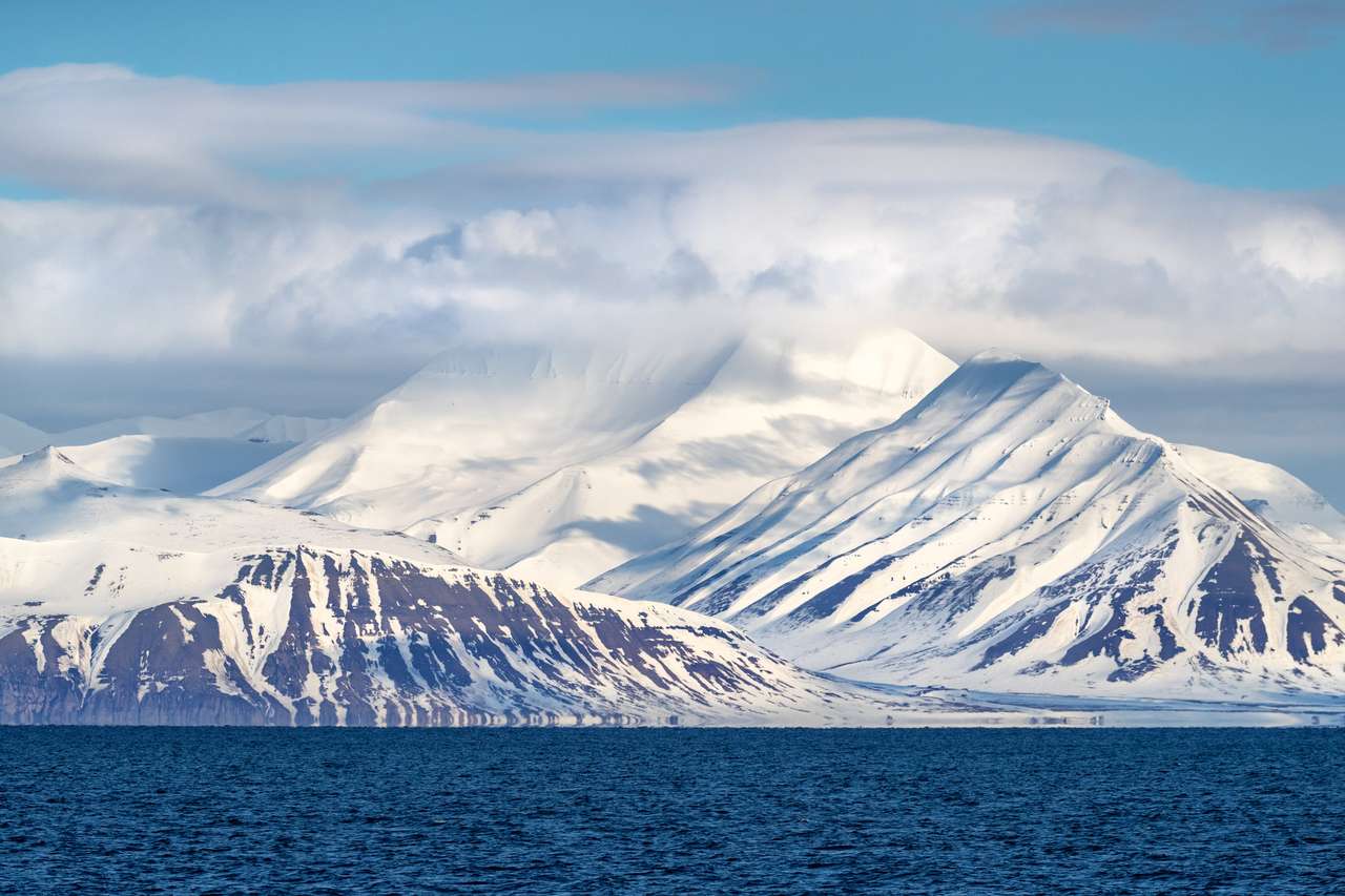 Broer Referendum trimmen De ongerepte en ongerepte sneeuw bedekte bergen van Svalbard stijgen uit de  ijzige blauwe wateren van de fjord. Svalbard is een Noorse archipel tussen  het vasteland van Noorwegen en de Noordpool. -