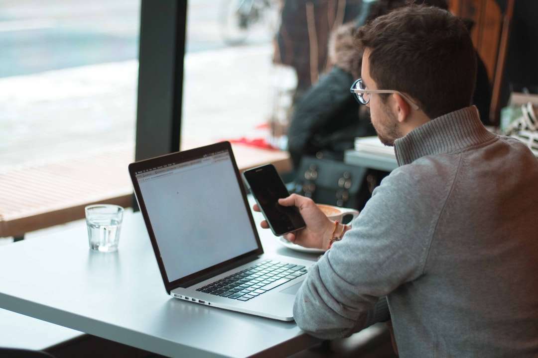 ember ül az asztal közelében, laptop és okostelefon kirakós online