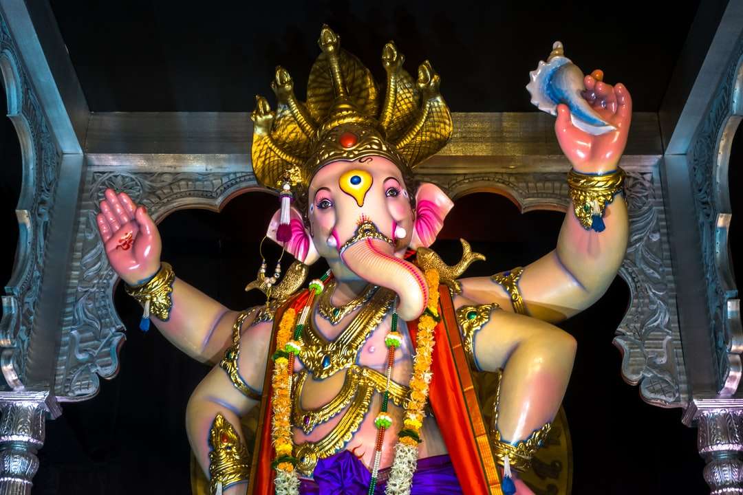 hinduistisk gudstaty framför guld och lila vägg pussel på nätet