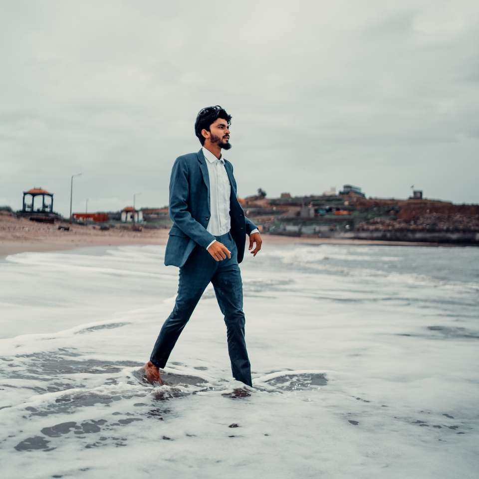 muž v modré džínové bundě stojící na pláži během dne online puzzle