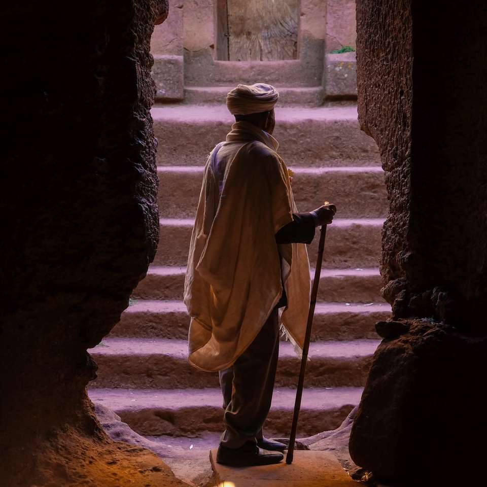 Mann, der auf braunem Steinhöhleneingang steht, während er Rohrstock hält Puzzlespiel online
