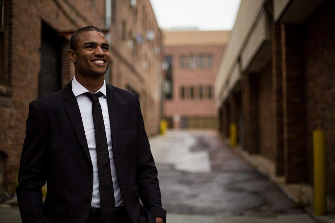 улыбающийся мужчина стоит между коричневыми бетонными зданиями онлайн-пазл