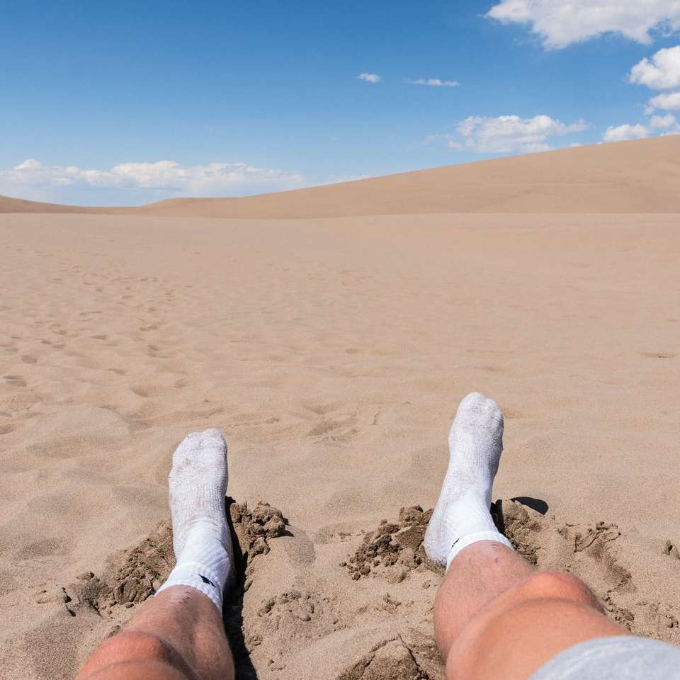 pessoa com meias brancas em pé na areia marrom durante o dia quebra-cabeças online