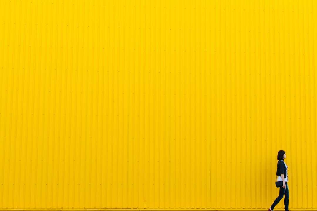 黄色の壁の近くに立っている黒いトップを着ている女性 ジグソーパズルオンライン