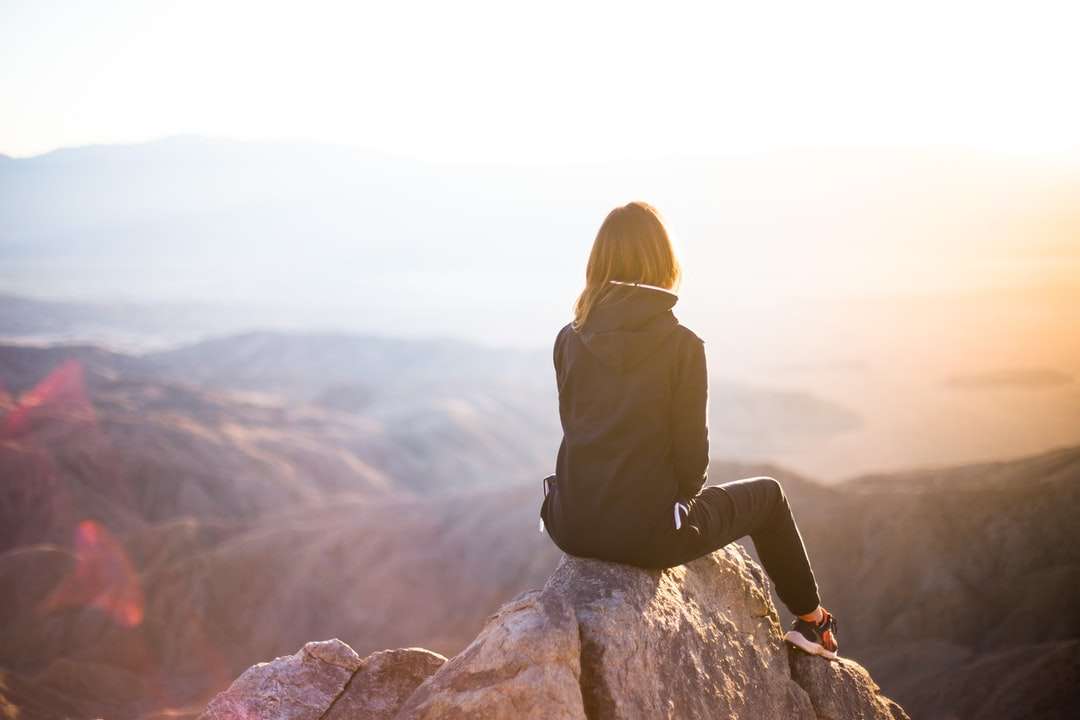 persoon zittend op de top van grijze rots met uitzicht op de bergen legpuzzel online