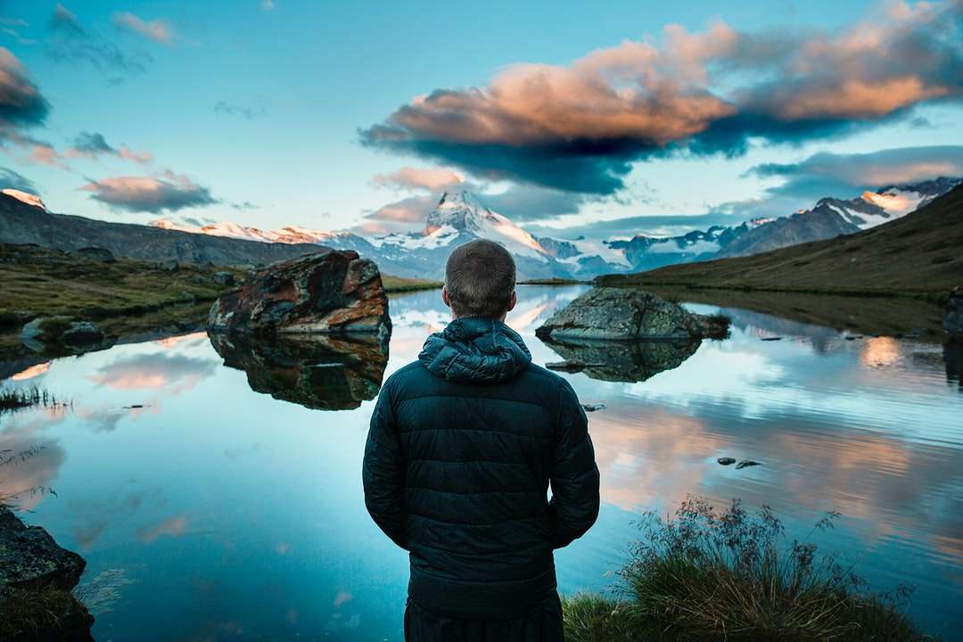 человек, стоящий перед видом на озеро, окруженное горами онлайн-пазл