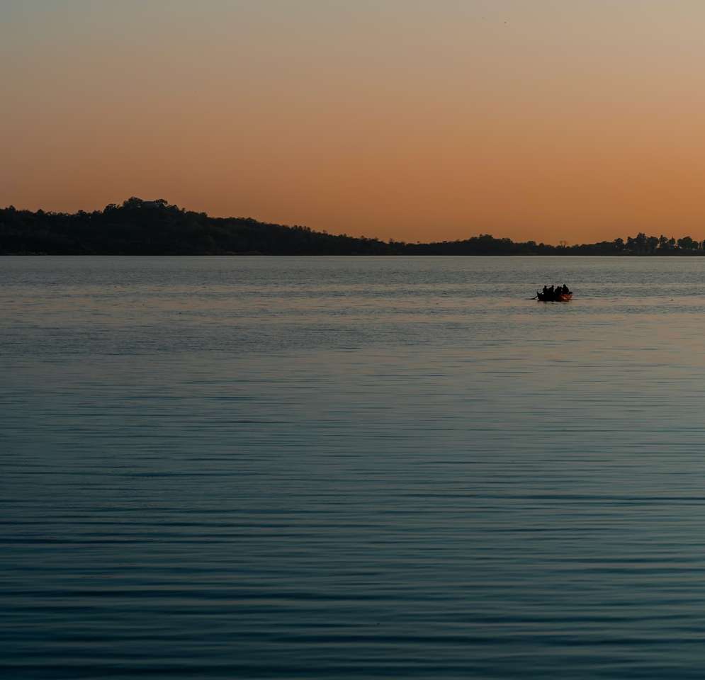 silueta de la persona que viaja en barco en el mar durante la puesta de sol rompecabezas en línea
