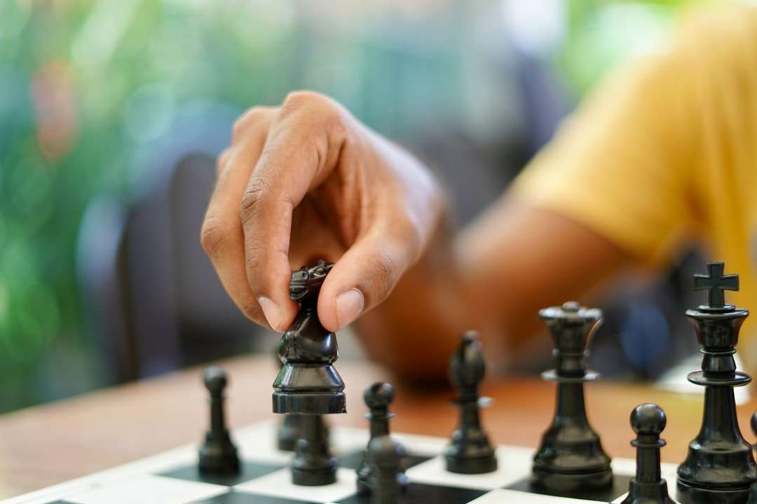 person holding black and silver chess piece online puzzle