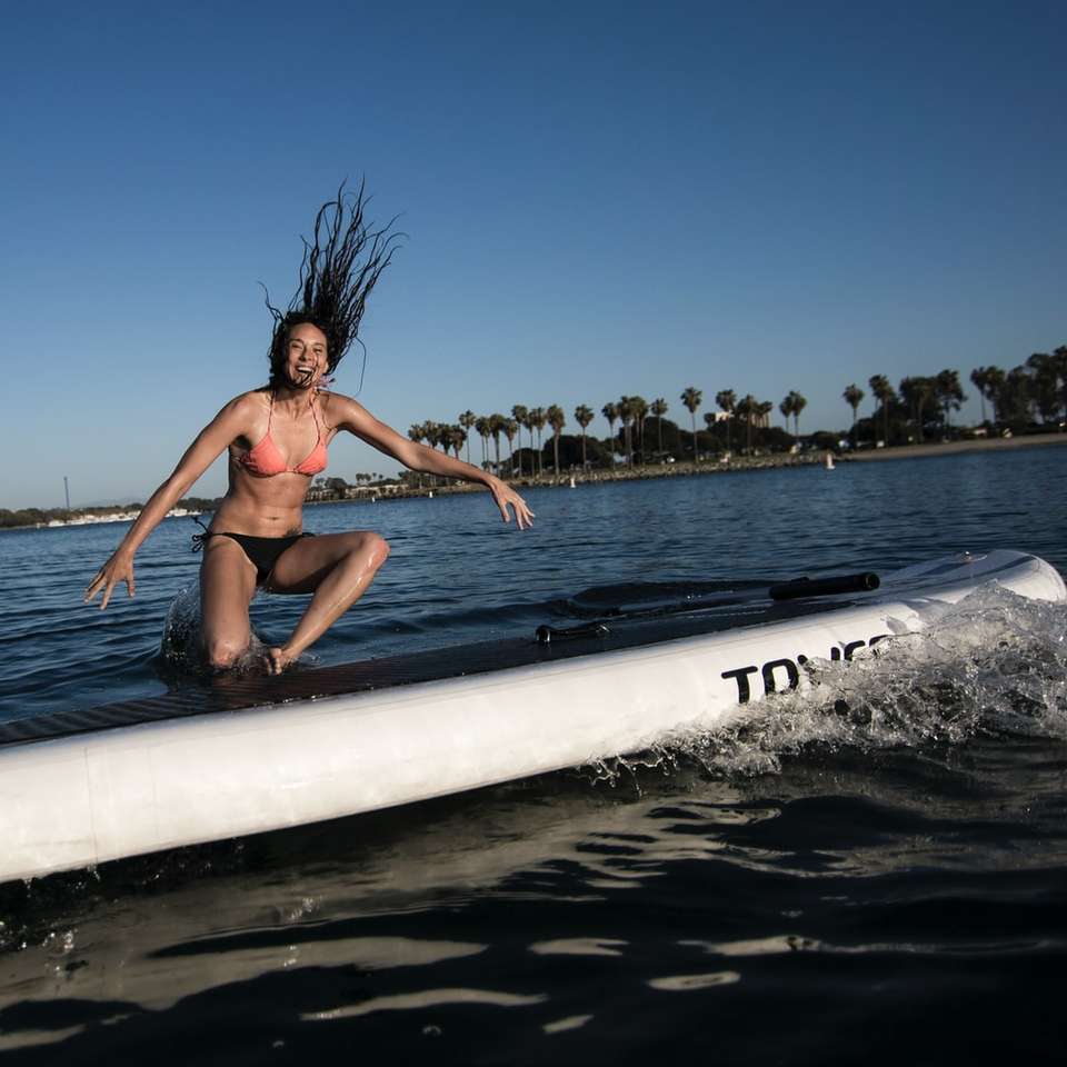 жена в син бикини, лежаща на бяла дъска за сърф в морето онлайн пъзел