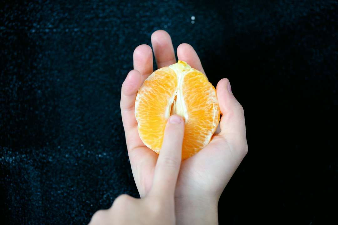 person som håller skivad orange frukt pussel på nätet