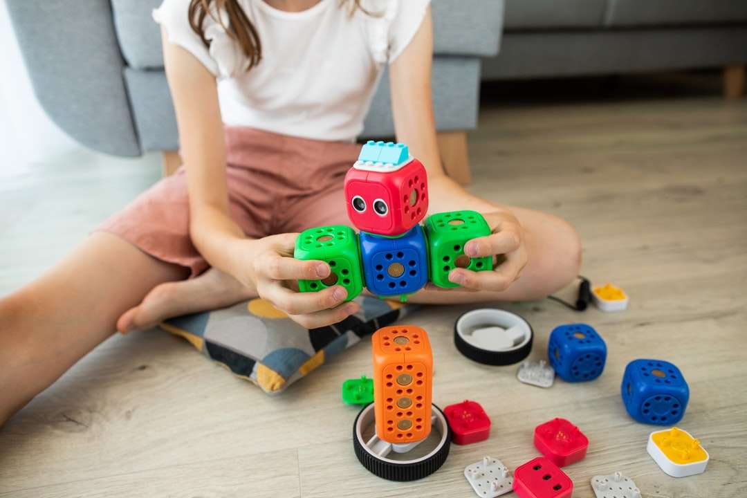 fille en chemise blanche jouant avec un jouet de voiture bleu et rouge puzzle en ligne