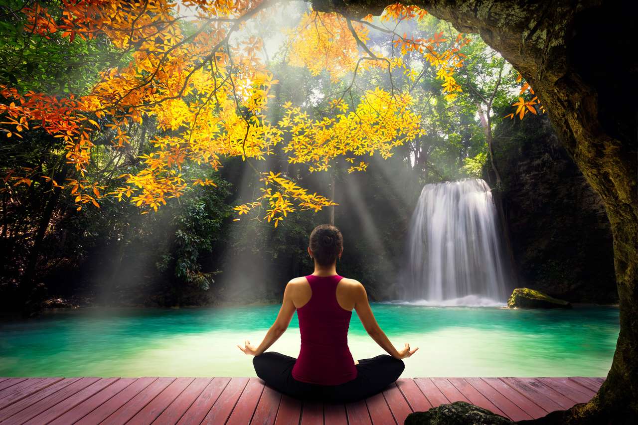 Mujer joven en pose de yoga sentada cerca de la cascada rompecabezas en línea
