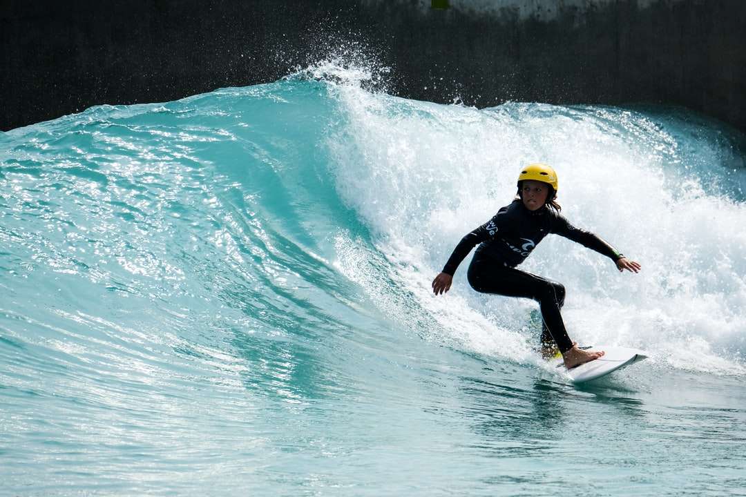 мъж в черен мокър костюм, каращ жълта дъска за сърф по вода онлайн пъзел