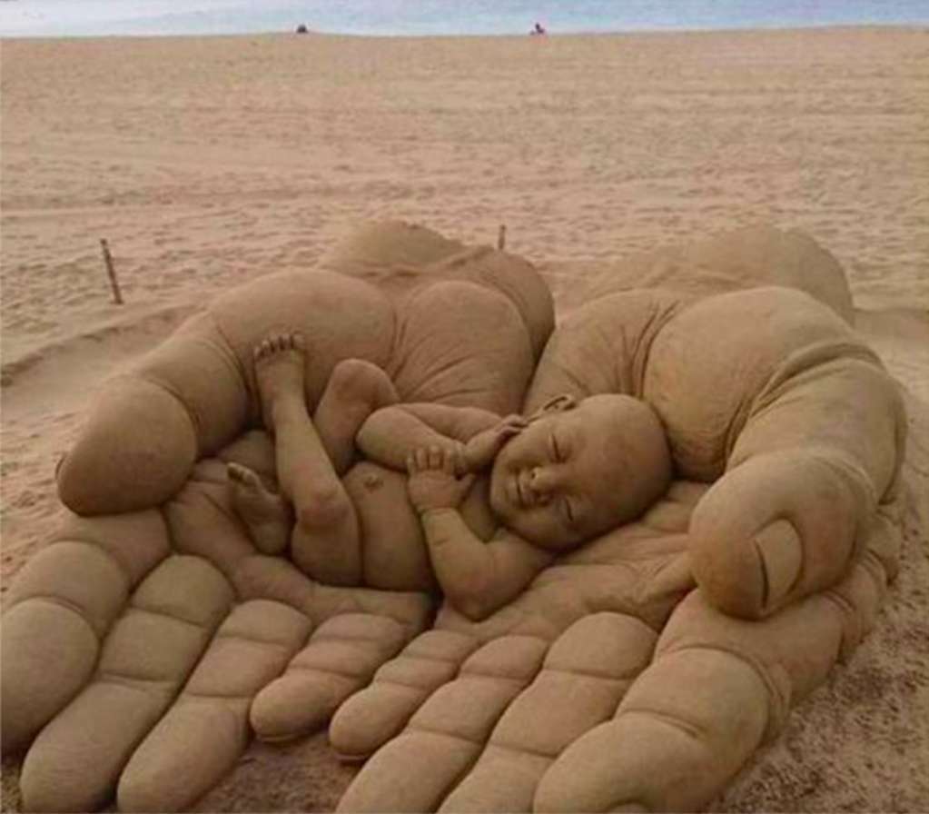 En sandskulptur av en baby i handflatan Pussel online
