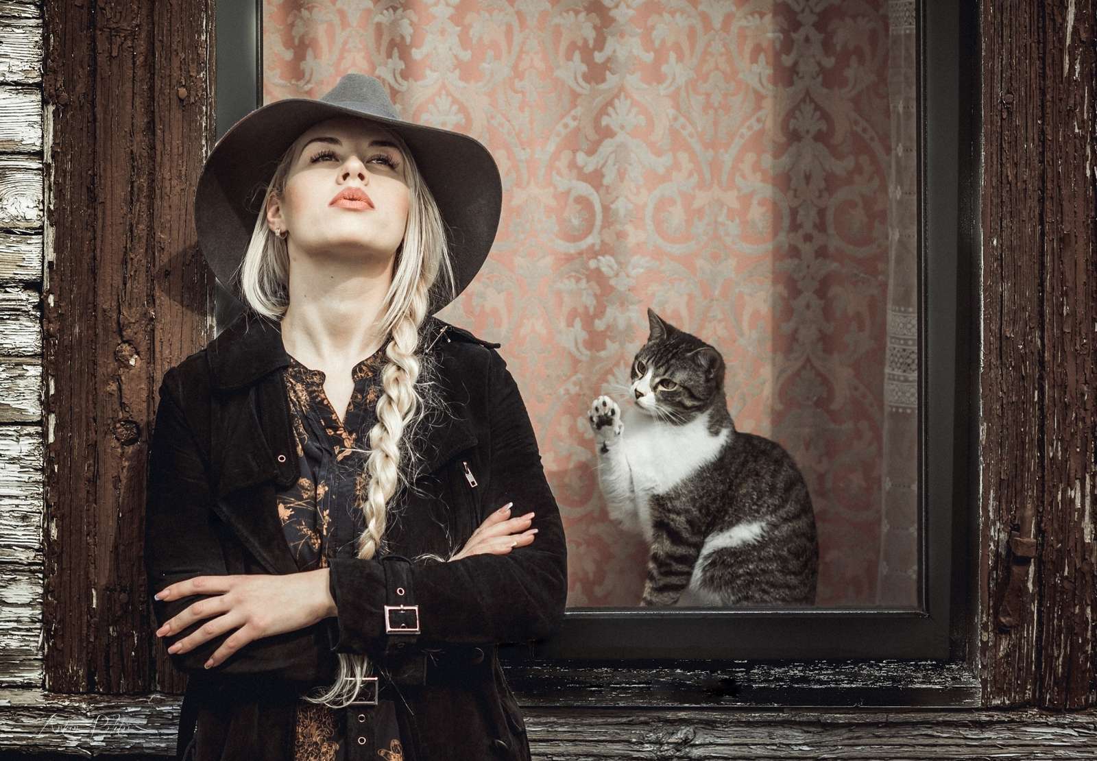 Blondhårig tjej i hatt och en kattunge utanför fönstret Pussel online